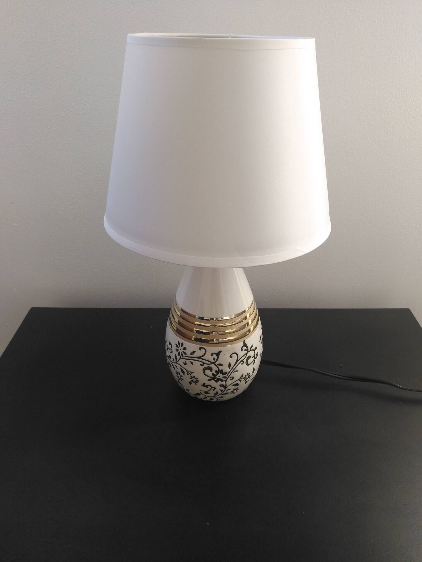 Een tafellamp met een witte kap en decoratieve voet.