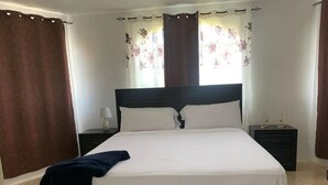 A bedroom with a large bed, dark headboard, white bedding, two bedside tables with lamps, and brown curtains.