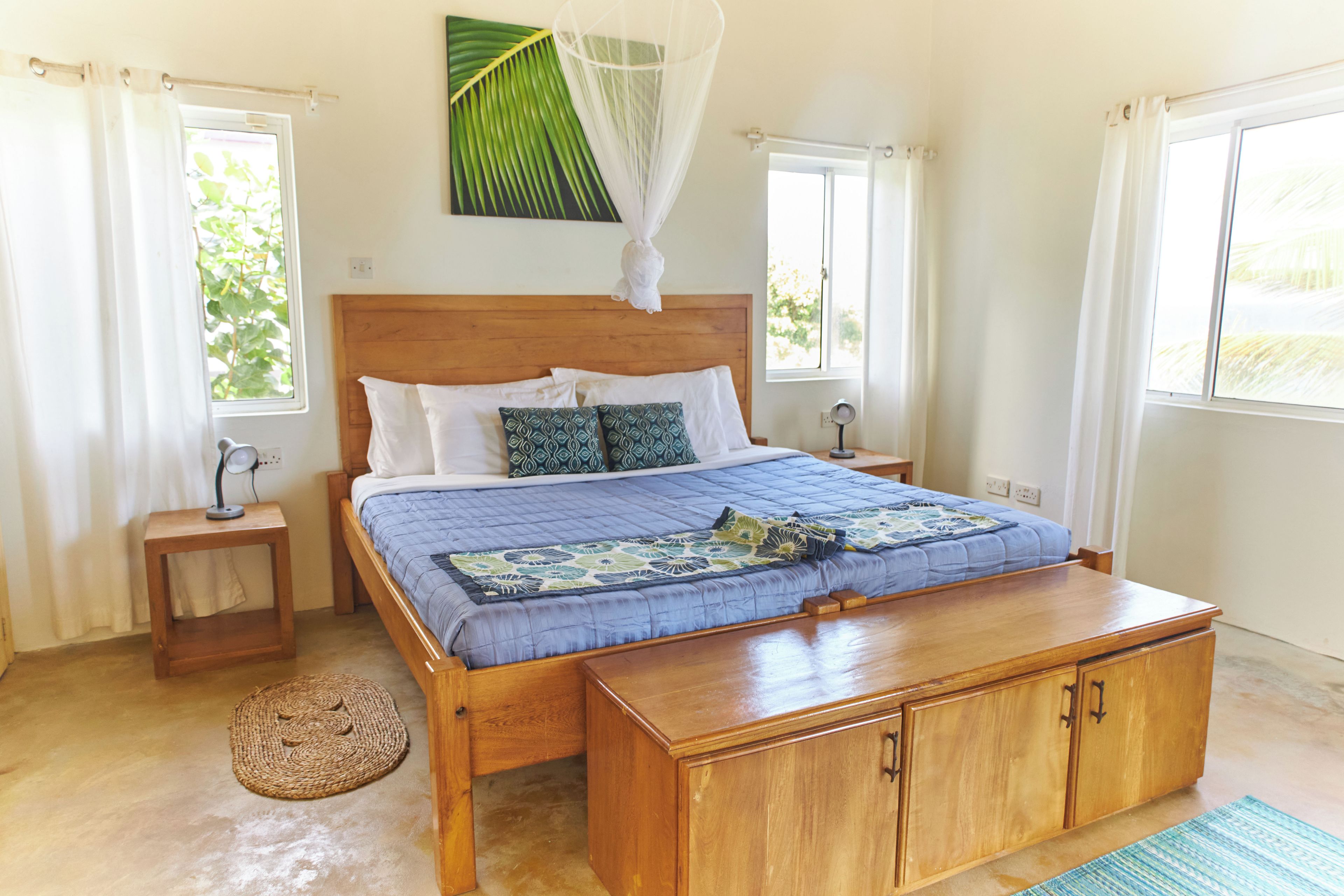 Ein Schlafzimmer mit einem hölzernen Bett, einem Nachttisch, einem Beistelltisch, einem gewebten Teppich und einem Baldachinbett.