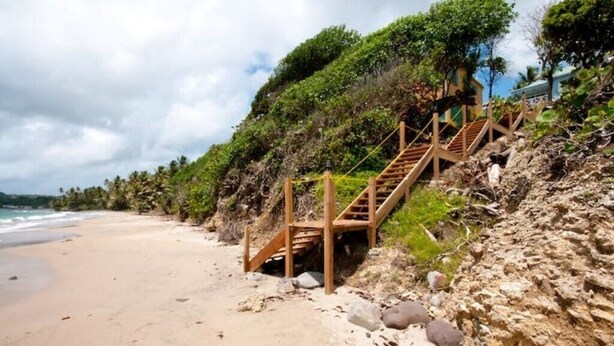 Une plage avec un escalier en bois menant au sommet d’une falaise rocheuse, d’où l’on a une vue sur l’océan.