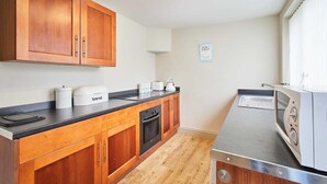 Une cuisine avec des meubles de rangement en bois, un plan de travail noir, un four à micro-ondes, un four traditionnel et un grille-pain.