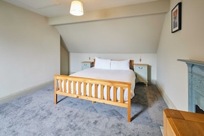 A bedroom with a wooden bed, two bedside tables, a white wall, and a blue fireplace. - Host & Stay | Moors Edge (Charltons)