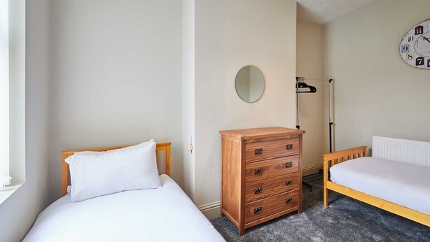 Une chambre avec deux lits, une commode, un miroir rond et une horloge murale.
