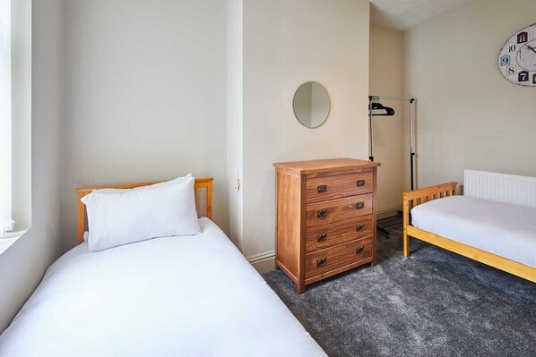 A bedroom with two beds, a dresser, a round mirror, and a wall clock.