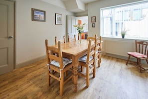 A dining area with a wooden table and chairs, a vase with flowers, and a window with blinds.