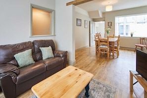 A living room with a brown leather sofa, a wooden coffee table, and a dining area with wooden chairs and a table. - Host & Stay | Moors Edge (Charltons)