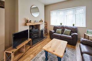 A living room with a TV on a wooden stand, a brown leather sofa, a wooden coffee table, and a fireplace with a mirror above it.