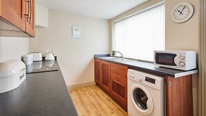 Une petite cuisine équipée d’un lave-linge, d’un four à micro-ondes et d’une horloge murale.