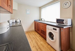 A compact kitchen with a washing machine, microwave, and a clock on the wall.