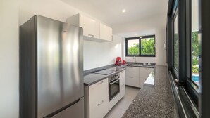A modern kitchen with stainless steel appliances, white cabinets, granite countertops, and a window providing a view of greenery outside. - Cute hideaway with private pool & garden. Close to nature & beaches. (Bonaire)