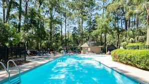 A swimming pool with a clear blue water, surrounded by lounge chairs and a small building.