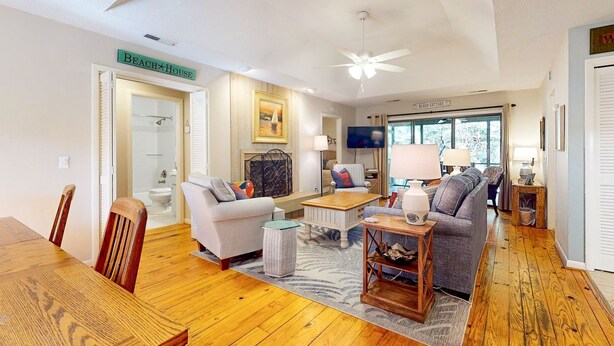 A spacious living room with a wooden floor, a ceiling fan, a sofa, a coffee table, and a TV.