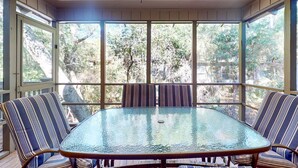 A covered patio with a glass table and striped chairs, large windows, and a ceiling fan.