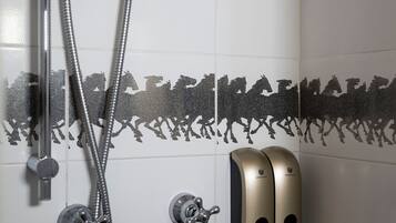 Un angolo doccia con soffione a mano, rubinetto a parete e dispenser per sapone.