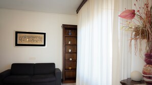 A living room with a black sofa, a wooden cabinet with shelves, a framed picture on the wall, and a vase with flowers on a side table.