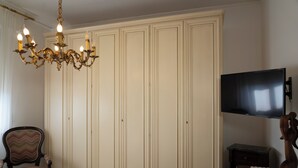 A room with a large wardrobe, a television, a wooden bench, and a patterned armchair.