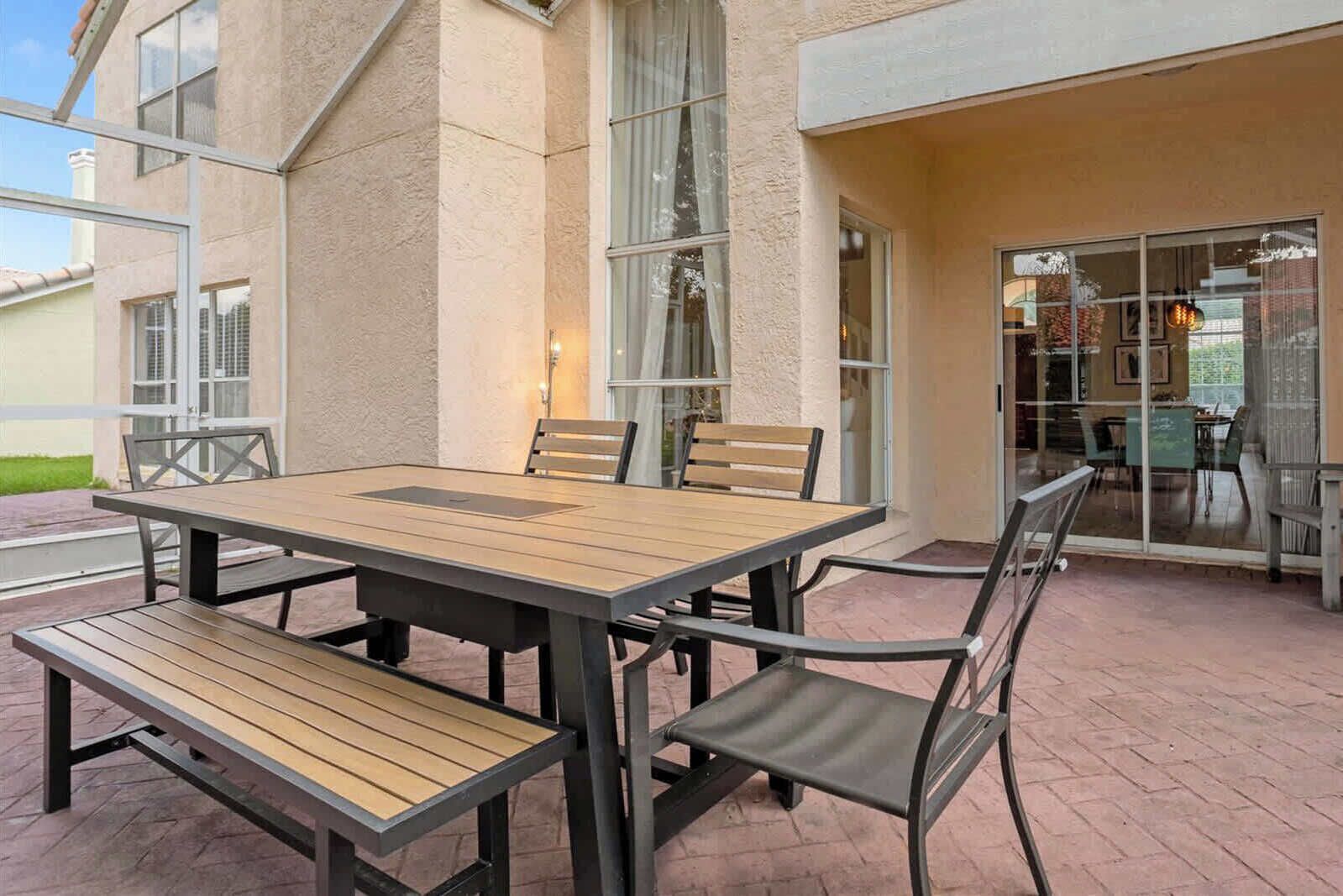 Eine Außenpatio mit einem Holztisch, Stühlen, einer Bank und einer Glastür zu einem Innenbereich.