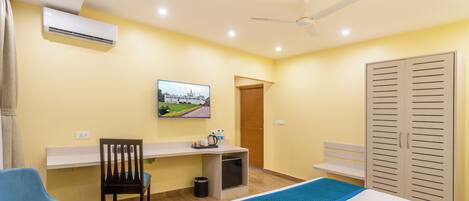 A hotel room with a bed, a desk, a chair, a TV, and a wardrobe.