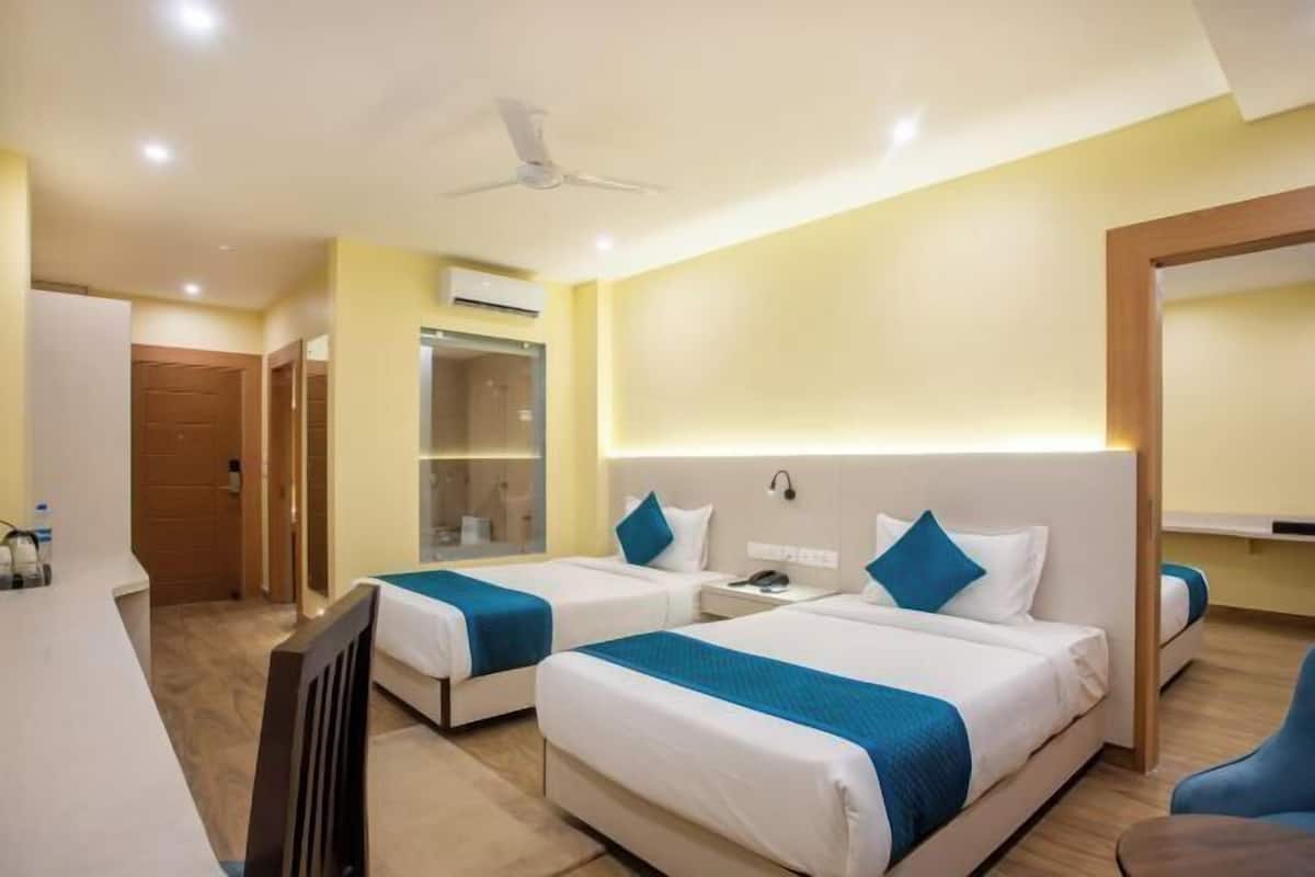 Une chambre d’hôtel avec deux lits, un bureau, une chaise, une armoire et un ventilateur de plafond.