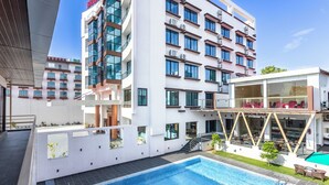 Un hotel moderno con piscina en la azotea, varios balcones y una zona de bar.