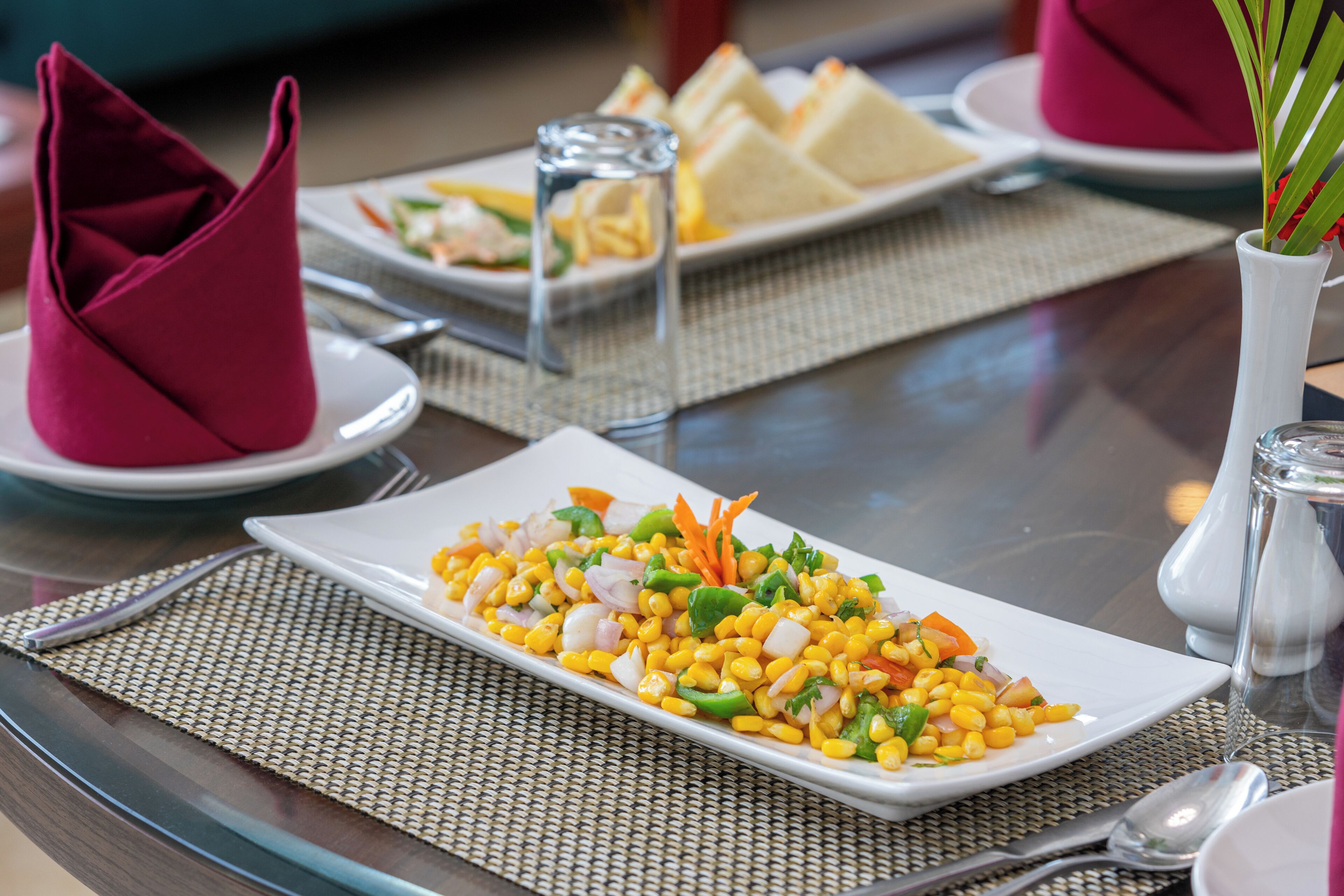 A dining table with a white plate of corn salad, a glass of water, and a napkin.