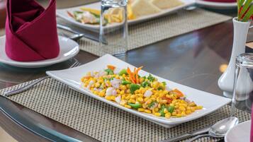 A dining table with a white plate of corn salad, a glass of water, and a napkin.