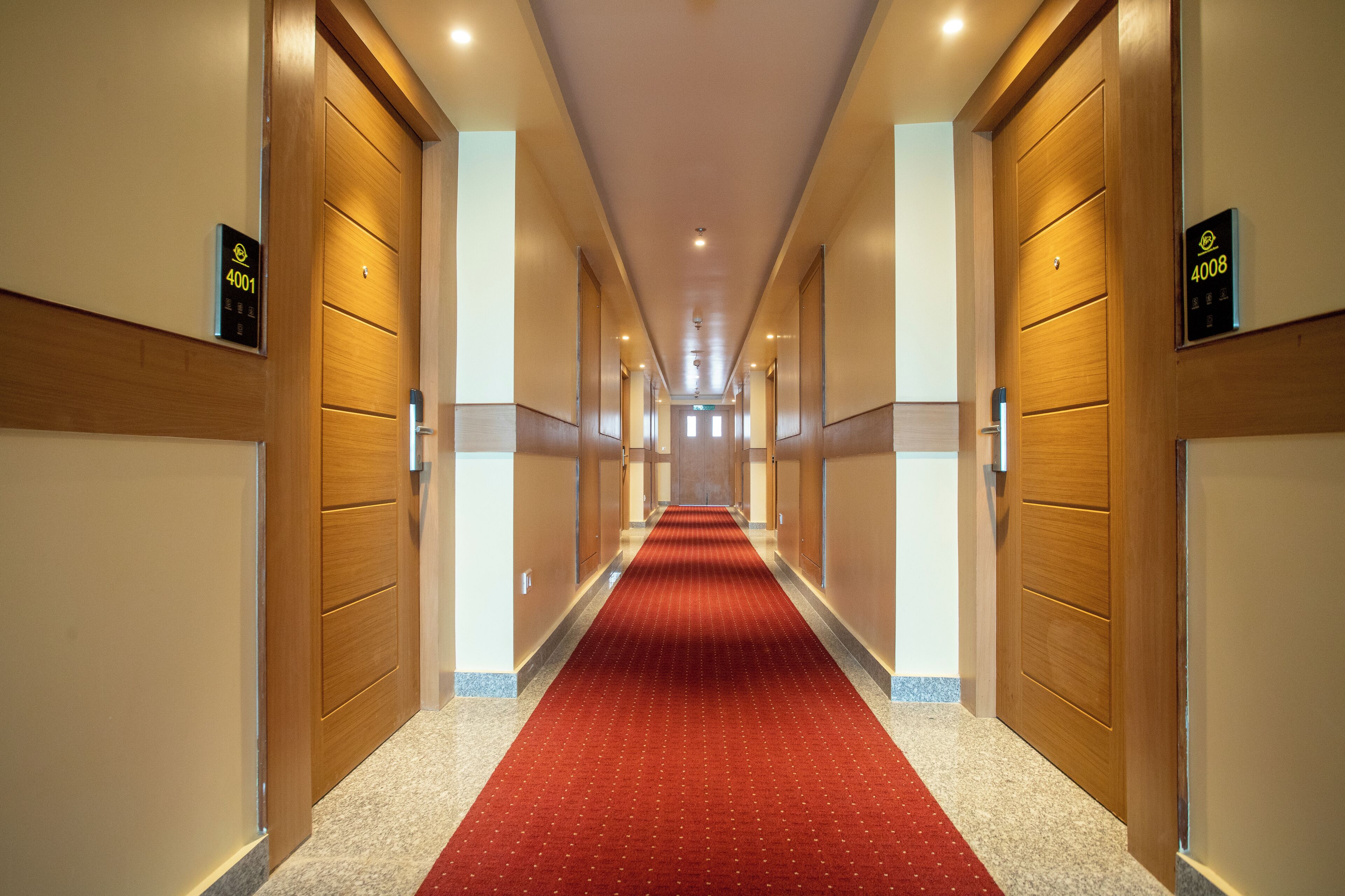 Un pasillo de hotel con alfombra roja, puertas de madera y letreros iluminados que indican los números de habitación 4001 y 4008.