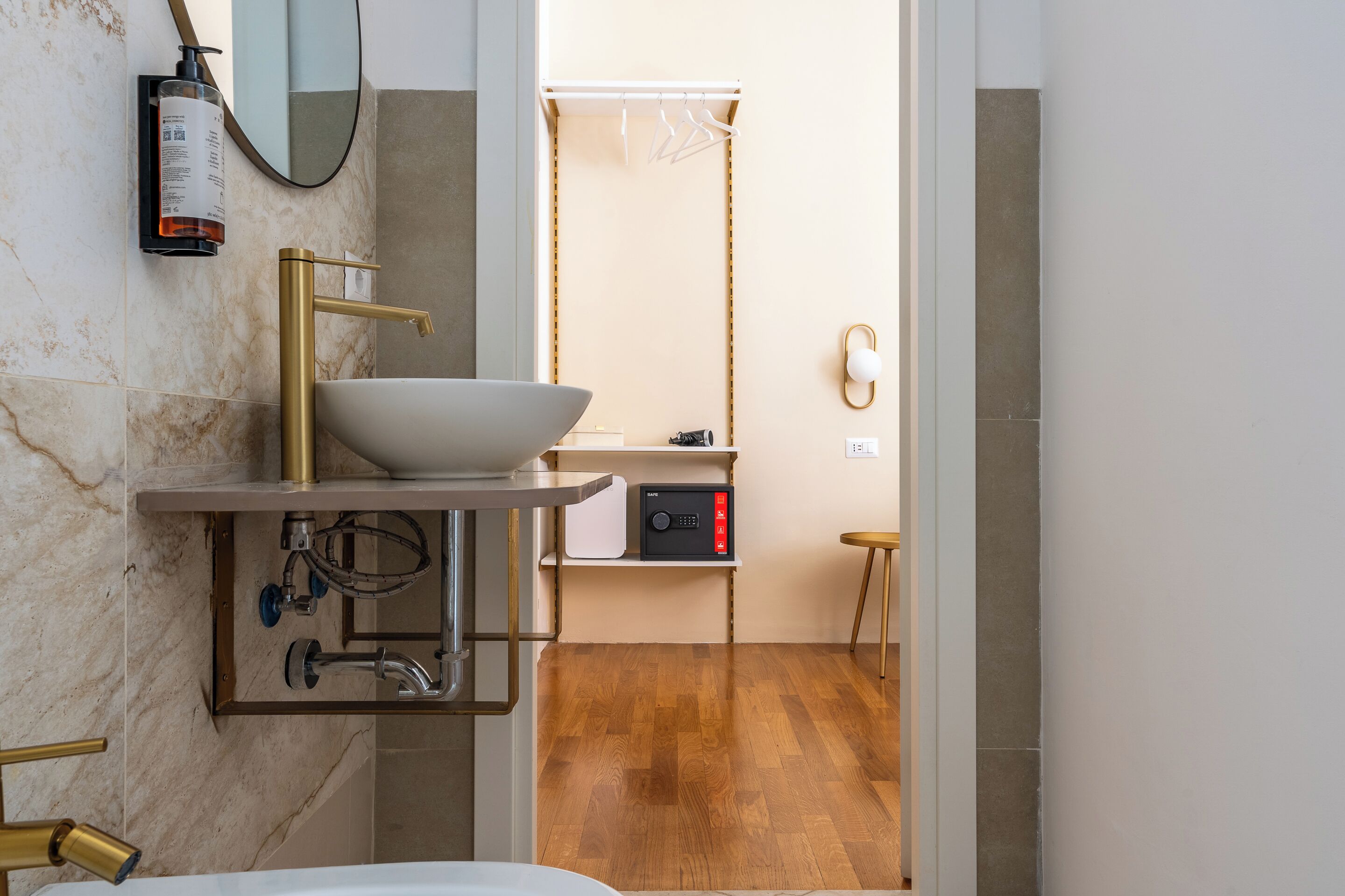 A modern bathroom with a marble wall, a gold faucet, a white sink, a handheld showerhead, a towel rack, a microwave, and a small round table.
