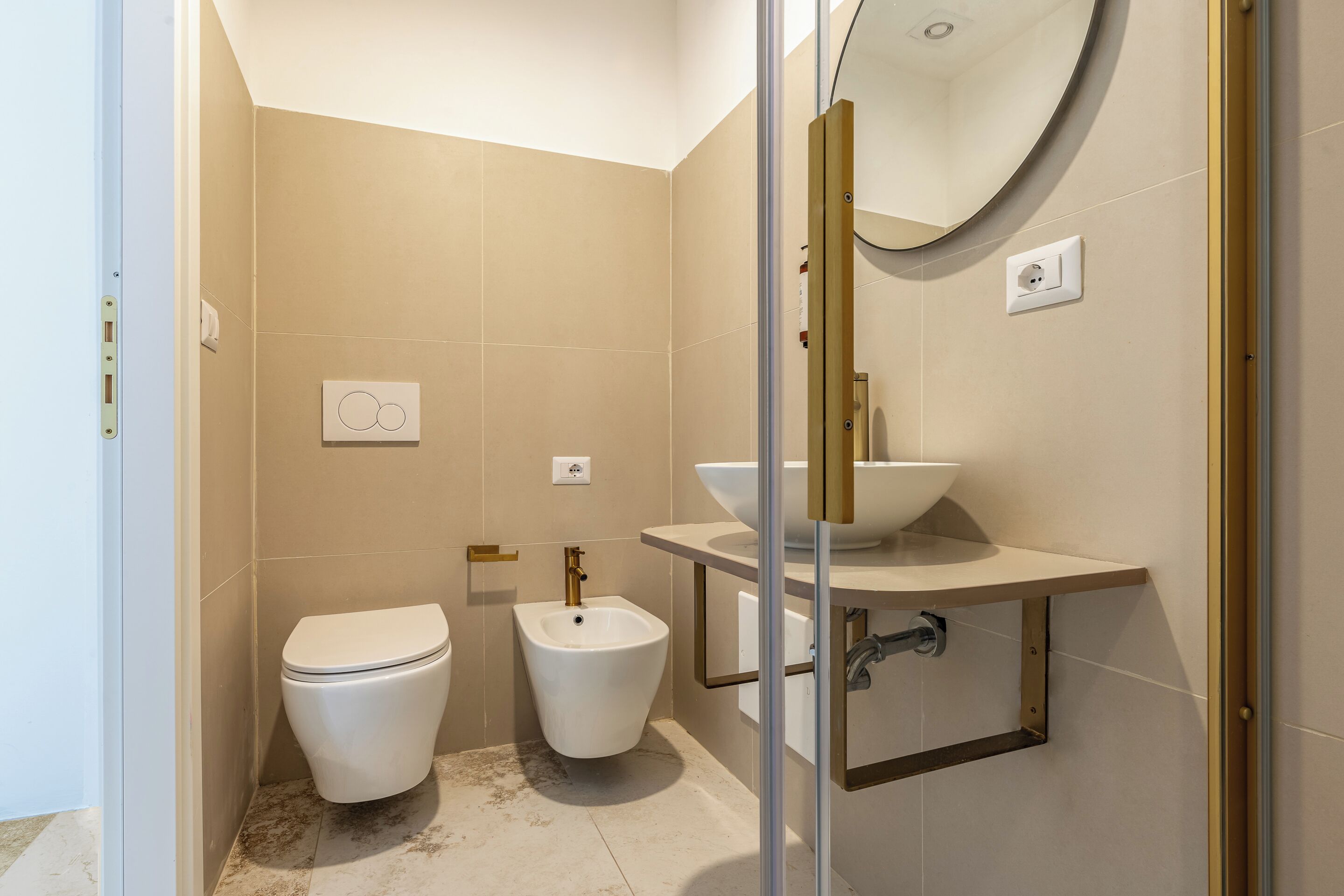 Un baño moderno con inodoro, bidé y un lavamanos grande con espejo superior.
