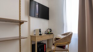 A hotel room with a flat-screen TV mounted on the wall, a wooden desk with a coffee maker, a chair, and a safe. - Decimo Meridio- At Spanish Steps- (Rome)