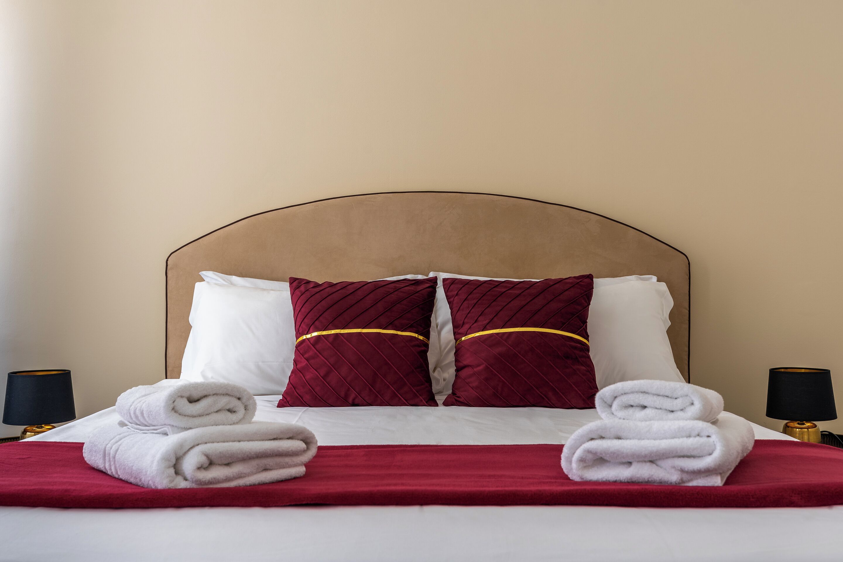 A neatly made bed with white linens, two red pillows, and a red throw blanket.