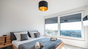 Ein modernes Schlafzimmer mit einem großen Bett, einem Holznachttisch, einer schwarzen Pendelleuchte und einem großen Fenster mit Blick auf die Stadt.