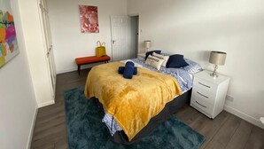 Een slaapkamer met een bed, nachtkastjes, een bankje en een deur.