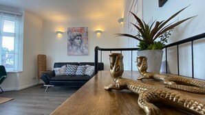 Een moderne woonkamer met een houten salontafel, een zwarte bank, een potplant en een lijst met een foto aan de muur.
