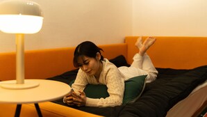 A person lying on a bed with a green pillow, a white lamp, and an orange wall. - Oak&Co (Seoul)