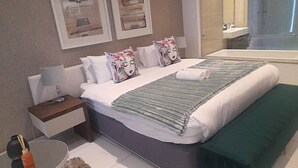 Habitació d'hotel moderna amb un llit gran, una taula de nit amb una làmpada i una banca verda.