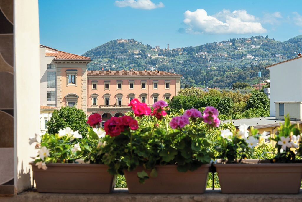 A balcony with potted flowers and a view of a hillside with buildings.