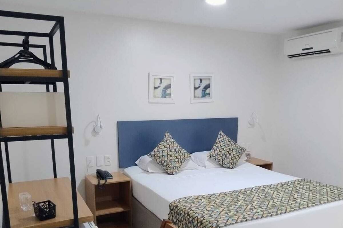 A hotel room with a bed, a desk, a chair, a wardrobe, and a wall-mounted air conditioner.