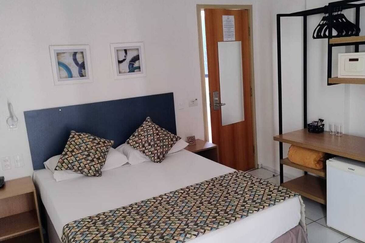 A hotel room with a bed, a desk, a chair, and a refrigerator.