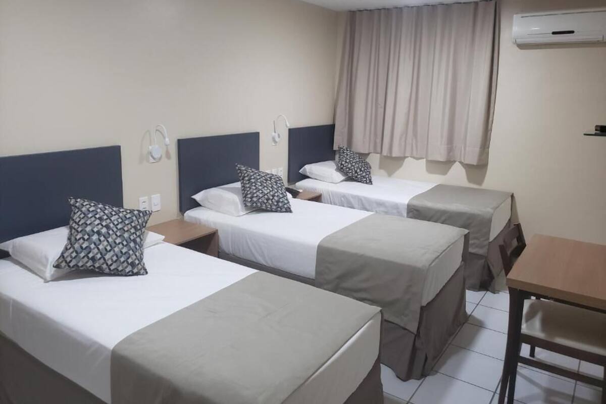 A hotel room with three single beds, a small table, and a chair.