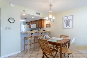 Un coin repas avec une table et des chaises en bois, un lustre, une horloge et une œuvre d’art représentant une tortue, encadrée, accrochée au mur.