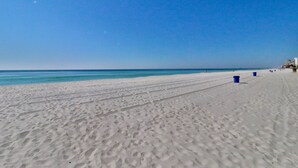 A wide sandy beach with footprints leading to the water, a clear blue sky, and a few buildings in the distance. - 2BR 2BA Penthouse Condo at the Long Beach! (Panama City Beach)