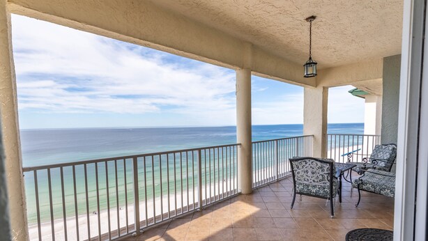 A balcony with a view of the ocean, a seating area with patterned furniture, and a hanging light fixture. - 2BR 2BA Penthouse Condo at the Long Beach! (Panama City Beach)