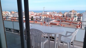 Un balcone con tavolo e sedie, vista su un paesaggio urbano con edifici e il mare.