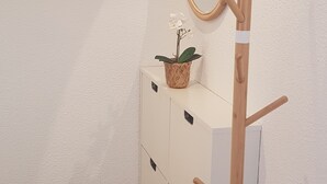 Un angolo di una stanza con un comò bianco, un appendiabiti in legno e una piccola pianta in vaso.
