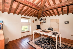Ein Zimmer mit Holzboden, einem Schachbrett auf einem Tisch, einem Schreibtisch, einem Stuhl, einem Fenster und einem Teppich.