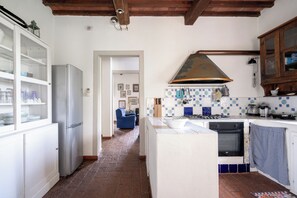 A kitchen with a refrigerator, stove, and oven, a blue chair, and a tiled backsplash.
