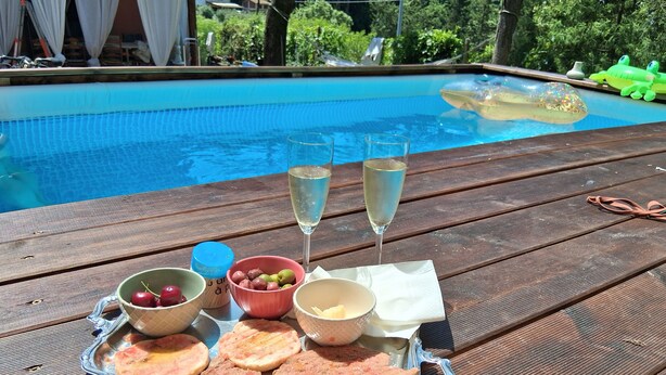 A wooden table with a tray of food, two glasses of champagne, and a pool in the background.