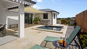 Un espace autour de la piscine comprenant une table et des chaises, un banc et un pot de fleurs.