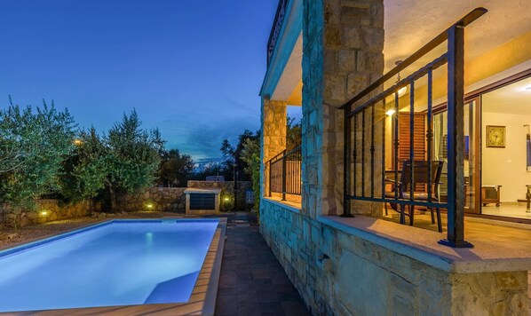 A stone building with a swimming pool, outdoor seating, and a stone wall.